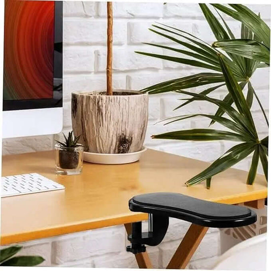 Ergonomic desk arm/wrist rest pad positioned next to a monitor and potted plants, enhancing workspace comfort.